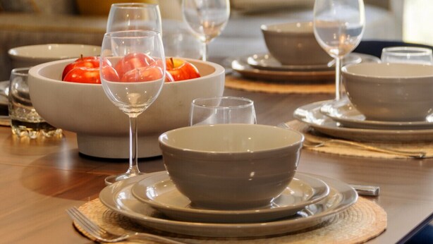Une table à manger dressée avec des bols, des assiettes et des verres à vin, avec un canapé et des coussins en arrière-plan.