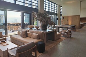 En rummelig opholdsstue med stor sofa, sofabord og en potteplante. Der er et spiseområde med bar og stole.