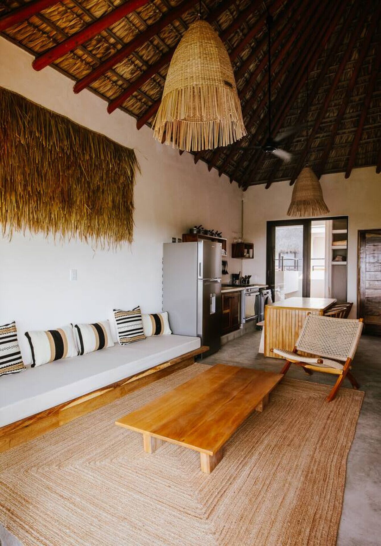 A spacious living area with a wooden coffee table, a sofa with patterned cushions, and a woven hanging light fixture.