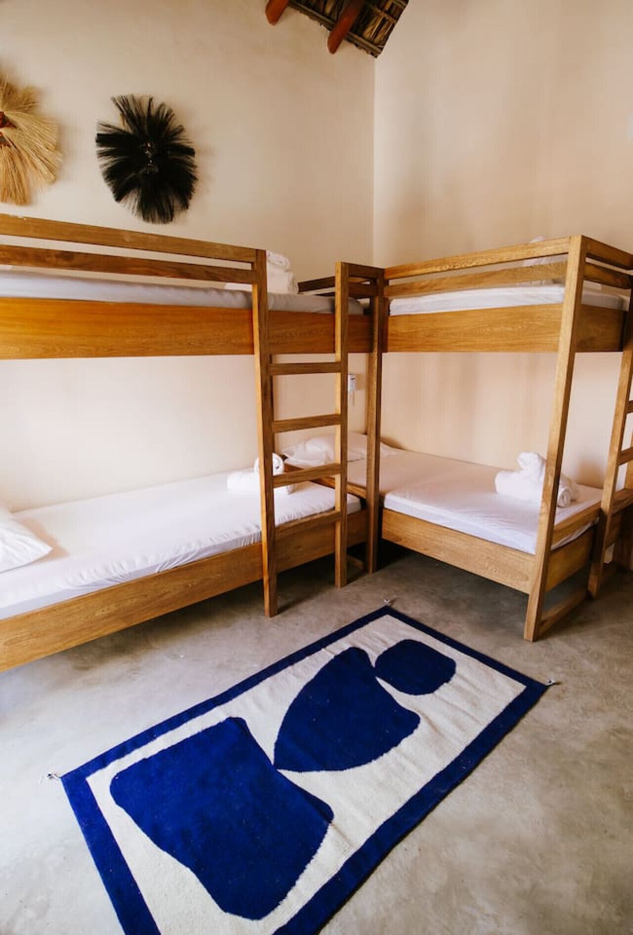 Una habitación con tres literas de madera, un tapete azul y blanco, y un adorno en la pared.
