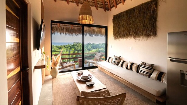 A modern living room with a large sliding glass door leading to a balcony with a scenic view. - Sunny 2 BR Penthouse w/ Priv. Jacuzzi & Balcony (La Barra)