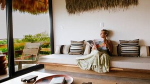 A cozy living room with a large window, a wooden coffee table, and a person reading a book. - Sunny 2 BR Penthouse w/ Priv. Jacuzzi & Balcony (La Barra)