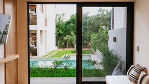 A modern room with a ceiling fan, a large sliding glass door leading to a pool and garden, a wooden table, and a sofa with cushions. - 2BR Beachside Escape with Private Terrace (La Barra)