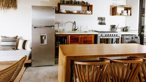 A kitchen with a wooden table and chairs, a refrigerator, a stove, and hanging utensils. - 2BR Beachside Escape with Private Terrace (La Barra)