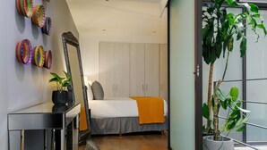 Ein modernes Schlafzimmer mit Bett, Nachttisch, Spiegel und einer Zimmerpflanze.