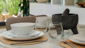Ein Essbereich mit einem für zwei Personen gedeckten Tisch, einschließlich Teller, Schüsseln, Gläsern und einem Mörser mit Stößel.
