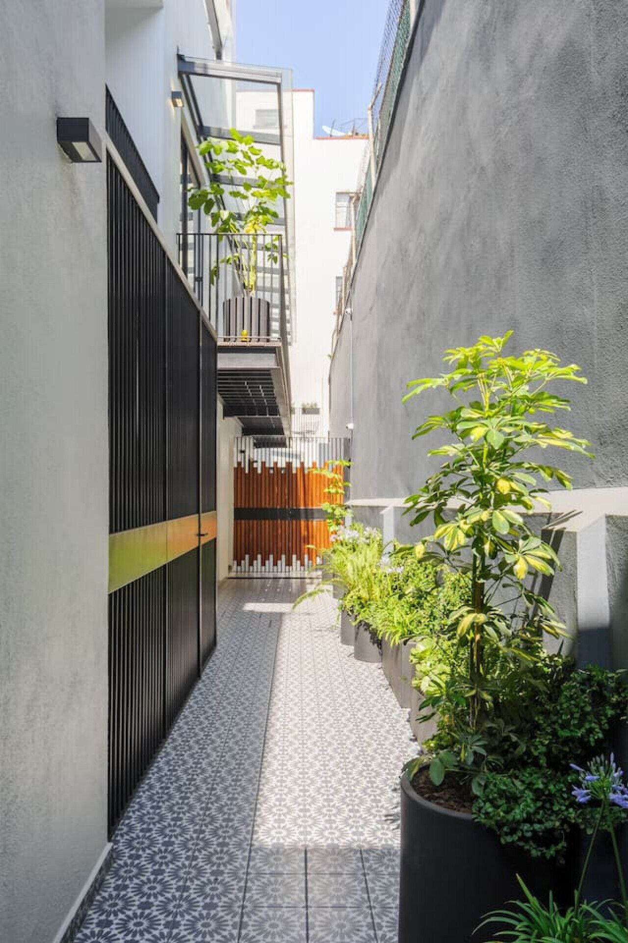 Une ruelle étroite, avec un sol carrelé, une porte noire et des plantes en pot.