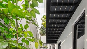 Um corredor estreito com piso de azulejos estampados, plantas em vasos e fachada de um edifício moderno.