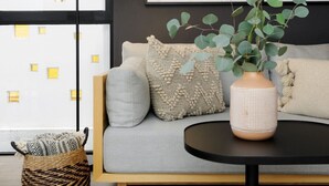 Uma sala de estar moderna com um sofá cinzento, uma cesta de vime e um vaso com folhas verdes.