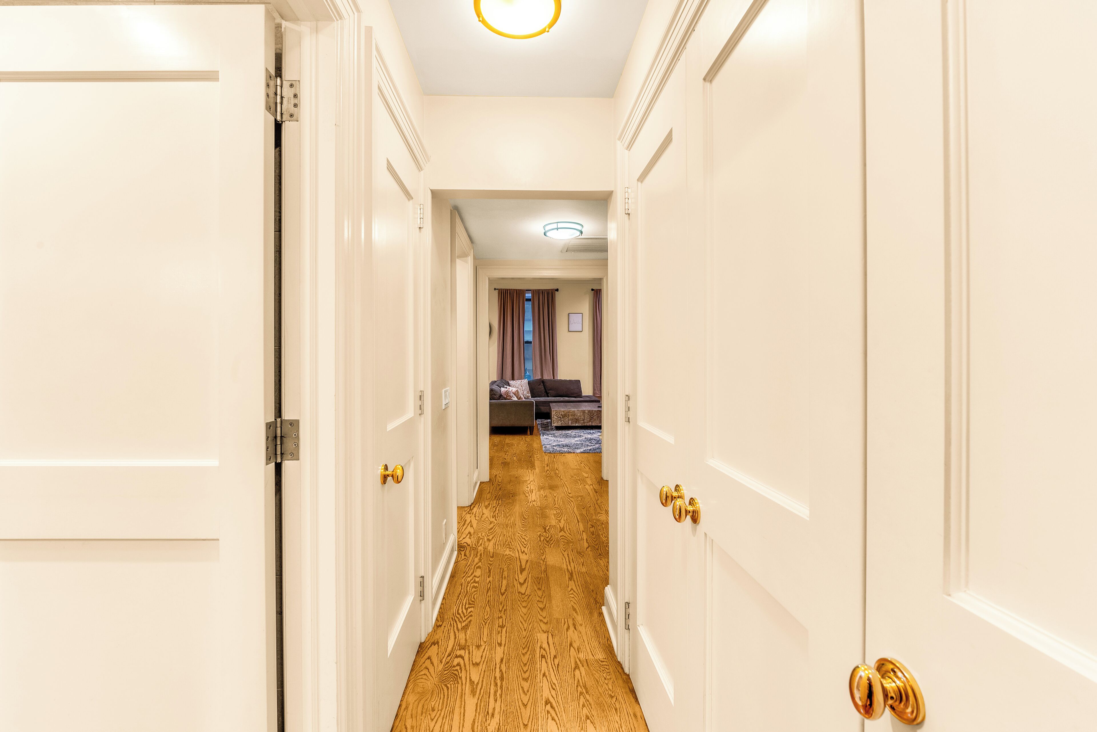 A hallway with white doors, a wooden floor, and a bed in the background.