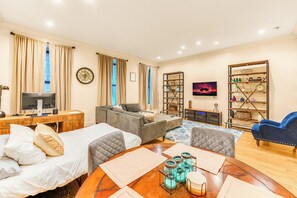A well-lit living room with a sofa, a dining table with placemats, a TV, and a bookshelf. - Massive Brownstonewith AC in Midtown NYC (New York)