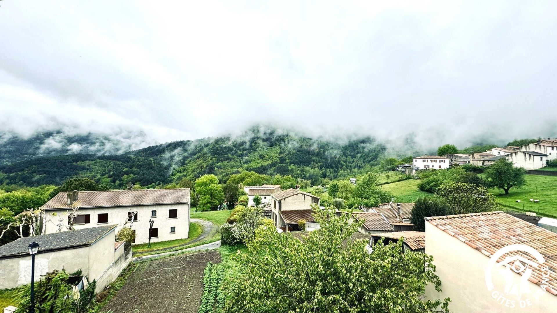 Ein ländliches Dorf mit traditionellen Gebäuden, freier Aussicht auf die umliegenden Hügel und einem Weg, der sich durch das Zentrum schlängelt.