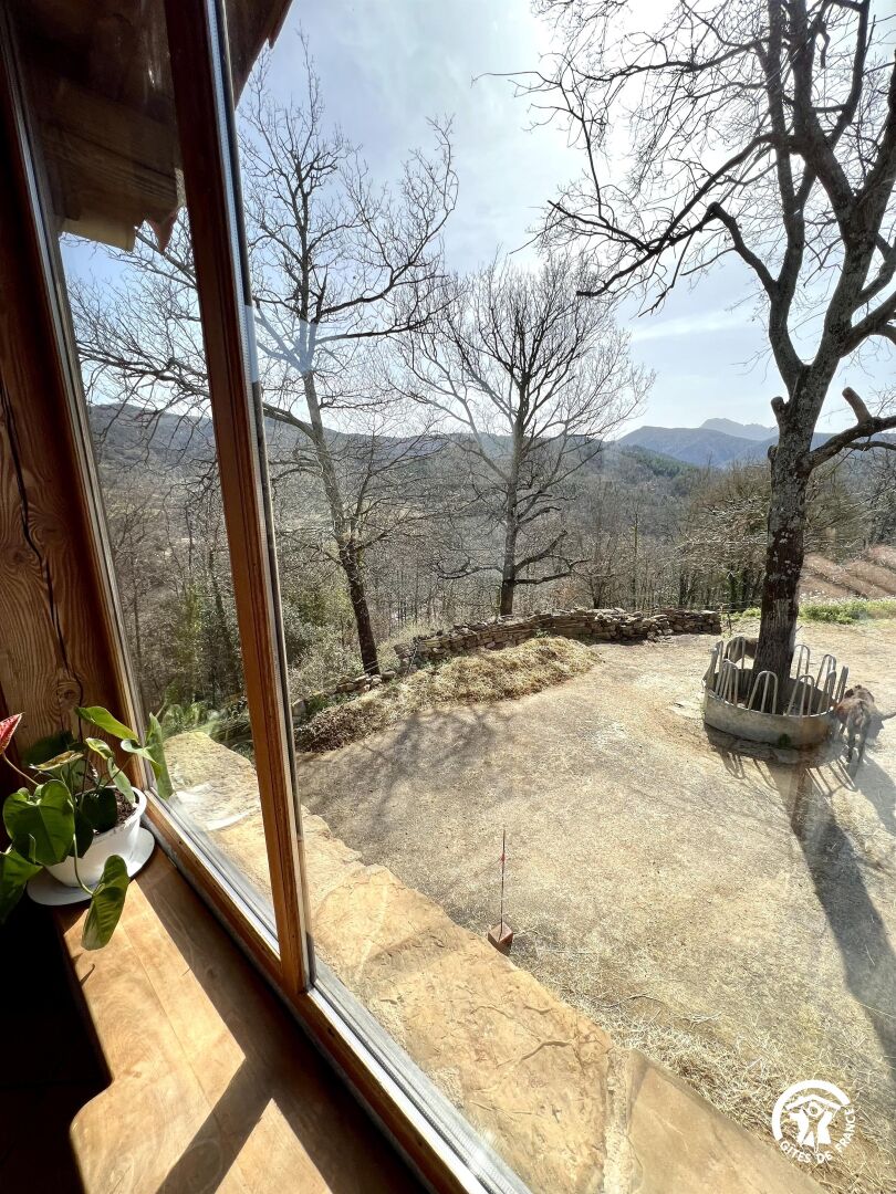 Blick aus einem Fenster auf eine trockene, hügelige Landschaft mit Bäumen und einem klaren Himmel.