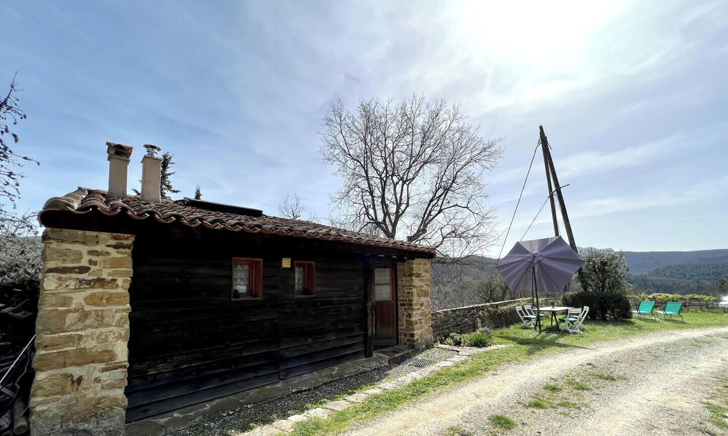 Un bâtiment rustique en bois, doté de piliers en pierre, d’un toit en métal et d’un moulin à vent en arrière-plan.