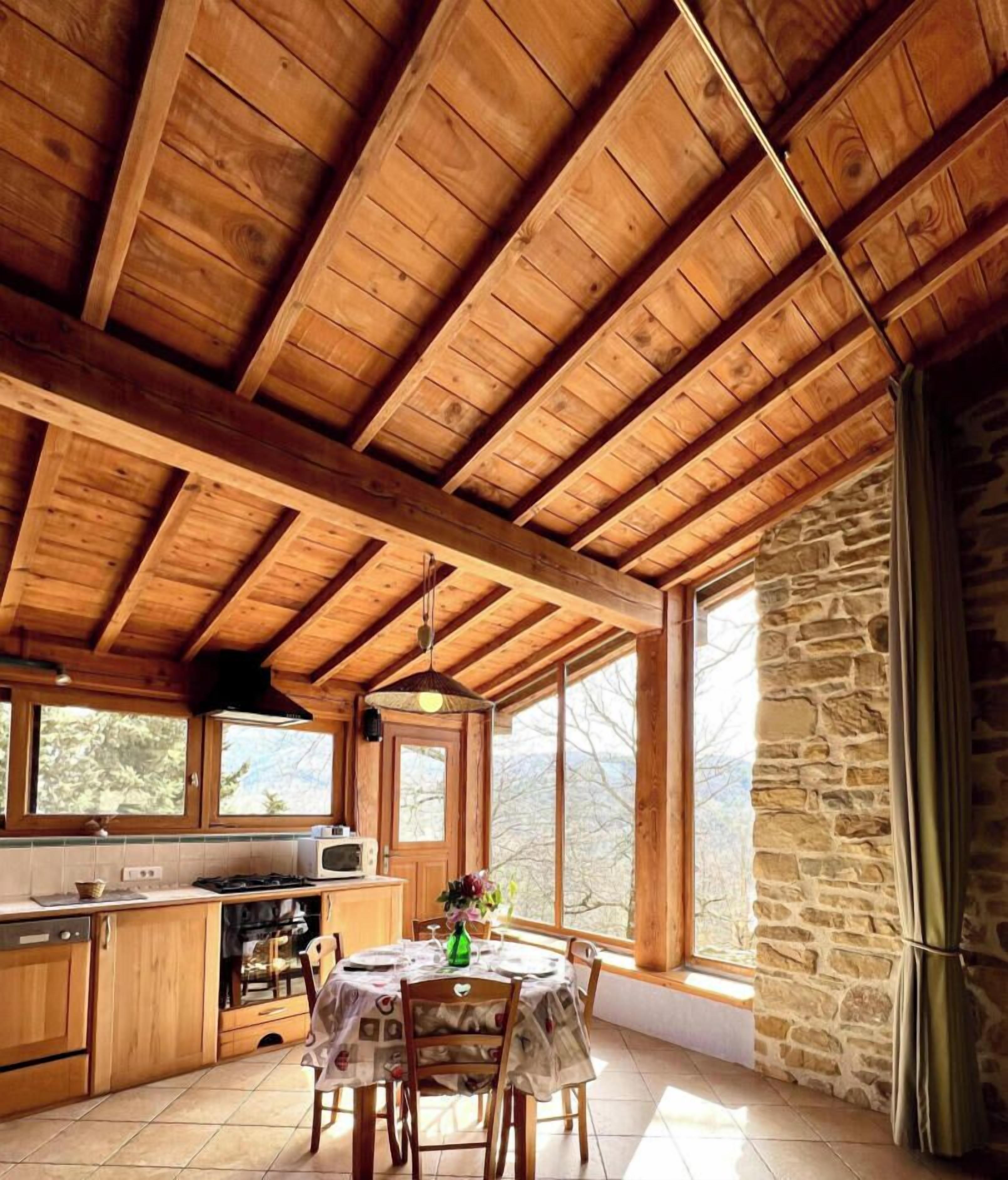 A wooden interior with a kitchen area, dining table, and large windows.