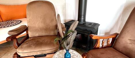 A cozy living area with two brown leather sofas, a small round table with a blue vase, and a black wood-burning stove.