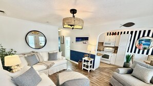 En moderne stue med sofa, skammel og spiseplads med et køkken i baggrunden.