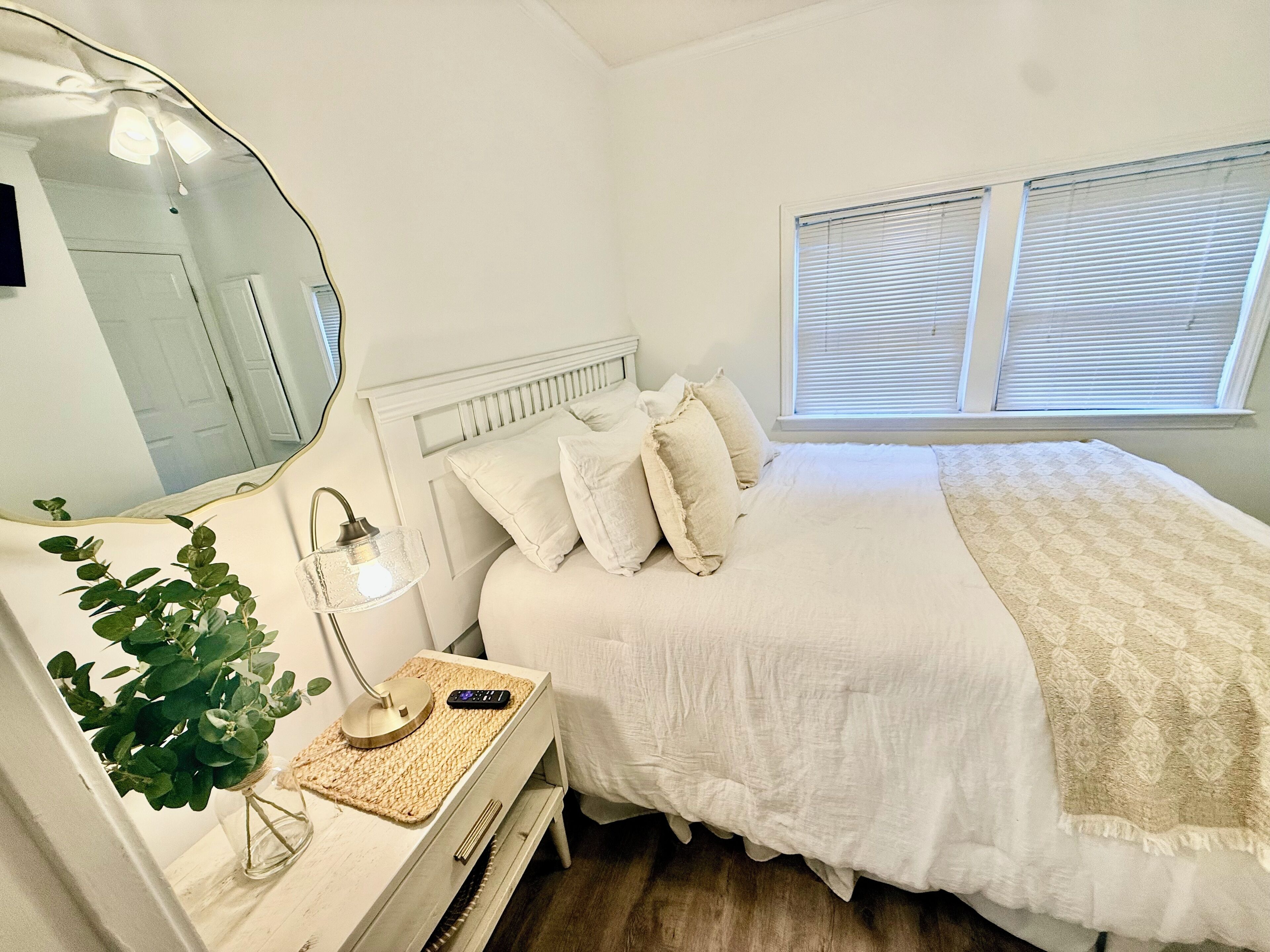 Een slaapkamer met een bed, nachtkastje, lamp en spiegel.
