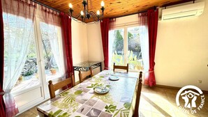 Un comedor con una mesa dispuesta para dos, una araña y vistas al jardín a través de amplios ventanales.