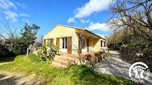 Una casa de dos pisos con fachada amarilla, contraventanas de madera y un camino de piedra que lleva a la entrada.