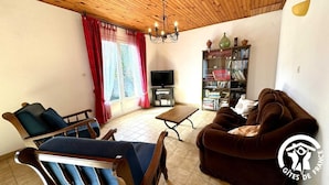 Una sala de estar con sofá, sillas, una mesa de centro, televisor y estantería.