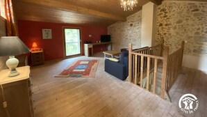 A spacious room with wooden flooring, a chandelier, a stone wall, and a balcony with a wooden railing. - Le Souleilla - SAINT JULIEN DE BRIOLA (SAINT JULIEN DE BRIOLA)