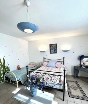 Un dormitorio con cama, mesitas de noche, escritorio, silla, lámpara colgante y una obra de arte en la pared.