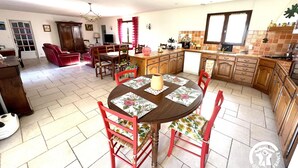 Ein geräumiges Wohnzimmer mit einem roten Ledersofa, einem Esstisch mit floralen Tischsets und einer Küche mit Holzausbau und einer gefliesten Rückwand.