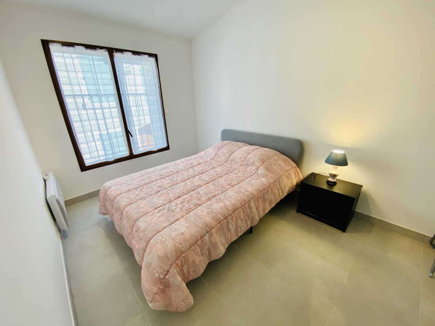 Een slaapkamer met een bed, nachtkastje, lamp en een raam met zonwering.