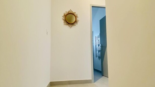 Ein schmaler Flur mit einem kleinen, dekorativen Spiegel an der Wand, der zu einer Tür am Ende führt.