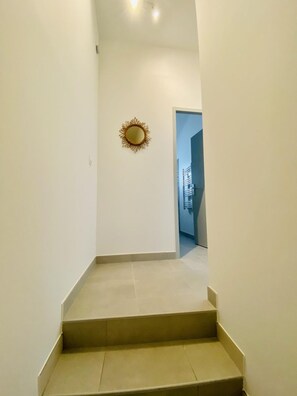 Un estrecho pasillo con un pequeño espejo decorativo en la pared, que conduce a una puerta al final.