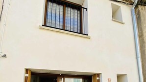 Ein Gebäude mit einem großen Eingang durch eine Schiebeglastür, einem kleinen Balkon darüber und einem geziegelten Dach.