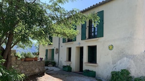 Un edificio de dos pisos con base de piedra, contraventanas verdes y camino de entrada de grava.