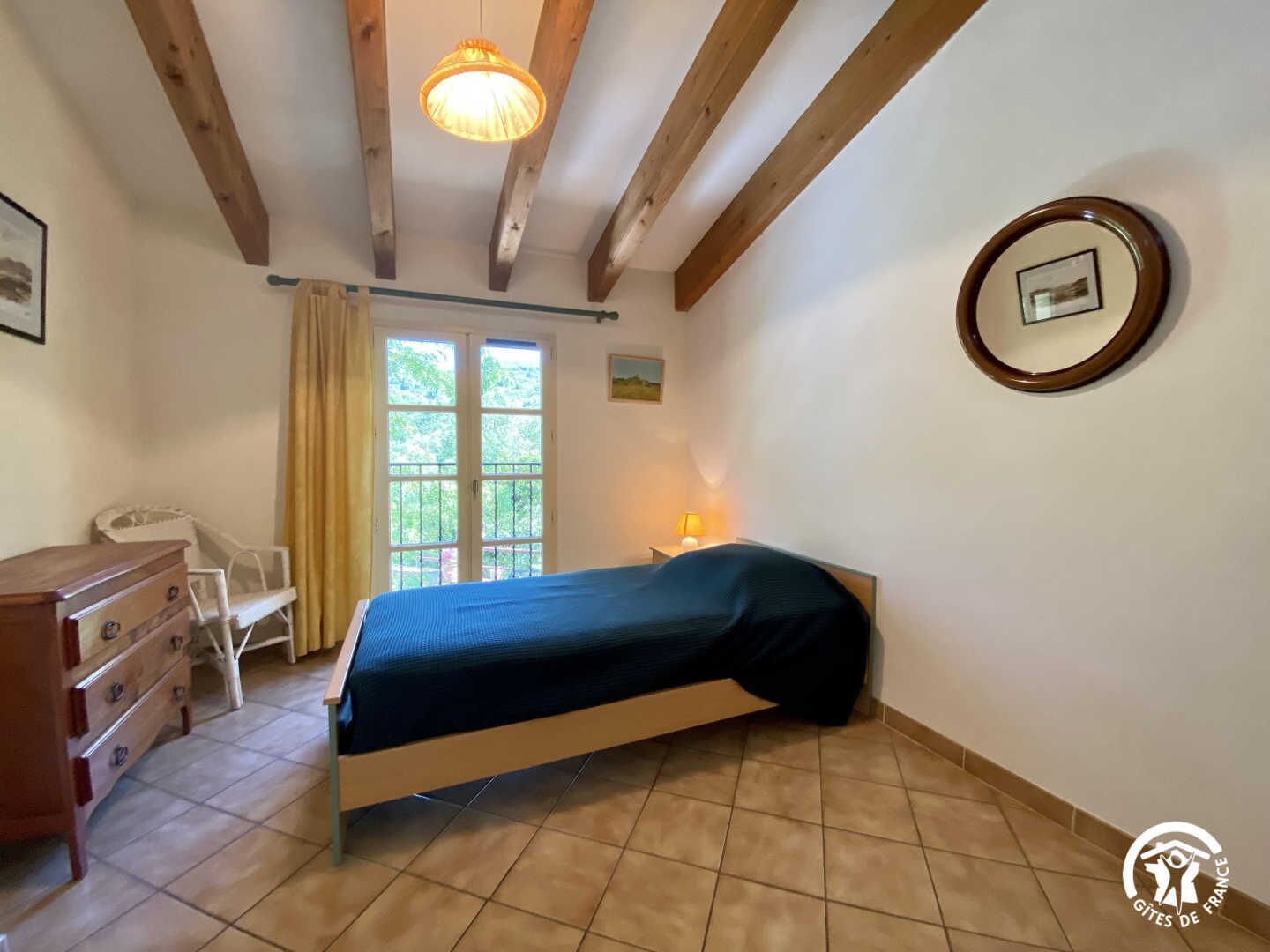 A bedroom with a bed, a dresser, a chair, a window with curtains, and a lamp.