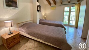 Un dormitorio con dos camas, una mesita de noche, una lámpara y una ventana con vistas a zonas verdes.