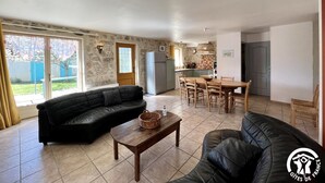 A living room with a black leather sofa, a wooden coffee table, and a dining area with a table and chairs. There is a kitchen area with a refrigerator and a window. - Le Vigneron - MONTGAILLARD (MONTGAILLARD)