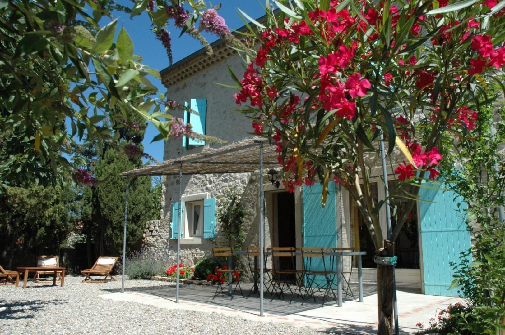 Un bâtiment en pierre doté d’un patio couvert, d’un espace extérieur aménagé pour s’asseoir et d’un jardin orné de fleurs rouges.