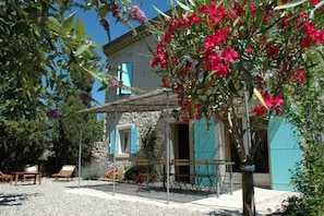 A stone building with a covered patio, outdoor seating, and a garden with red flowers.