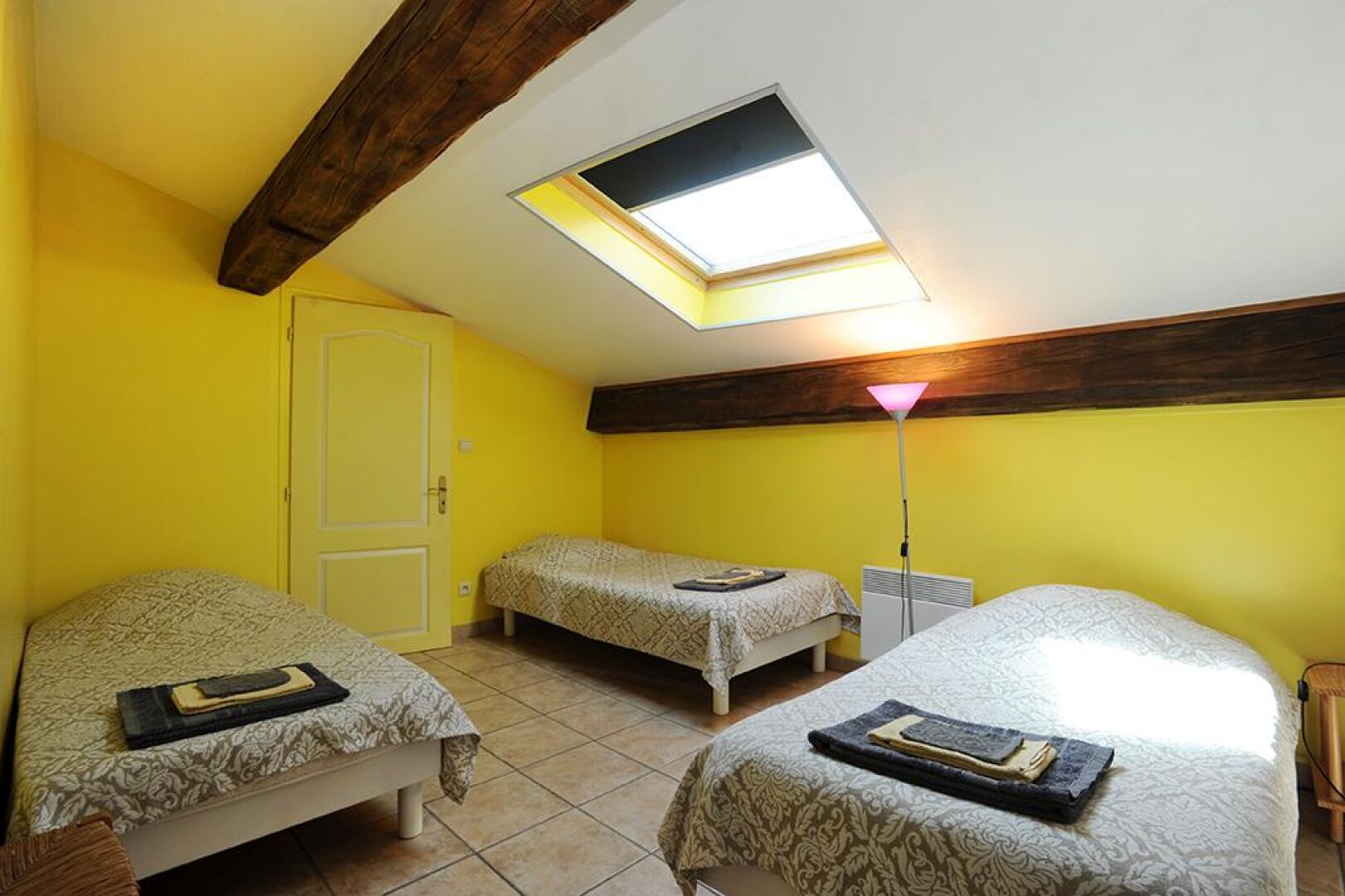 A dormitory room with two beds, a skylight, a standing heater, and a door.