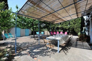 Eine Terrasse im Freien mit Esstisch, umgeben von Stühlen und einer Pergola, die Schatten spendet.