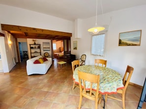 A spacious living area with a white sofa, a dining table with chairs, and a kitchen in the background. - Gite des Pesquis - BAGES (BAGES)