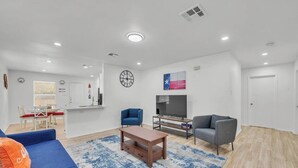 Un salon moderne avec un canapé bleu, une table basse, un téléviseur et une horloge au mur.