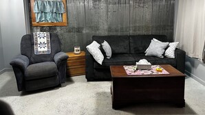 Un salon avec un canapé gris foncé, un fauteuil assorti, une table basse en bois et un ventilateur de plafond.
