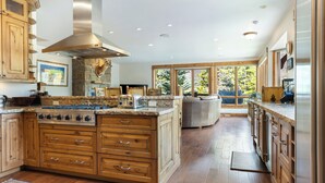 Une cuisine spacieuse avec des meubles en bois, un grand îlot central doté d’une cuisinière et une cheminée en pierre.