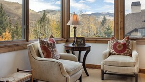 Une pièce chaleureuse avec deux fauteuils placés face à une grande fenêtre donnant sur un paysage montagneux.