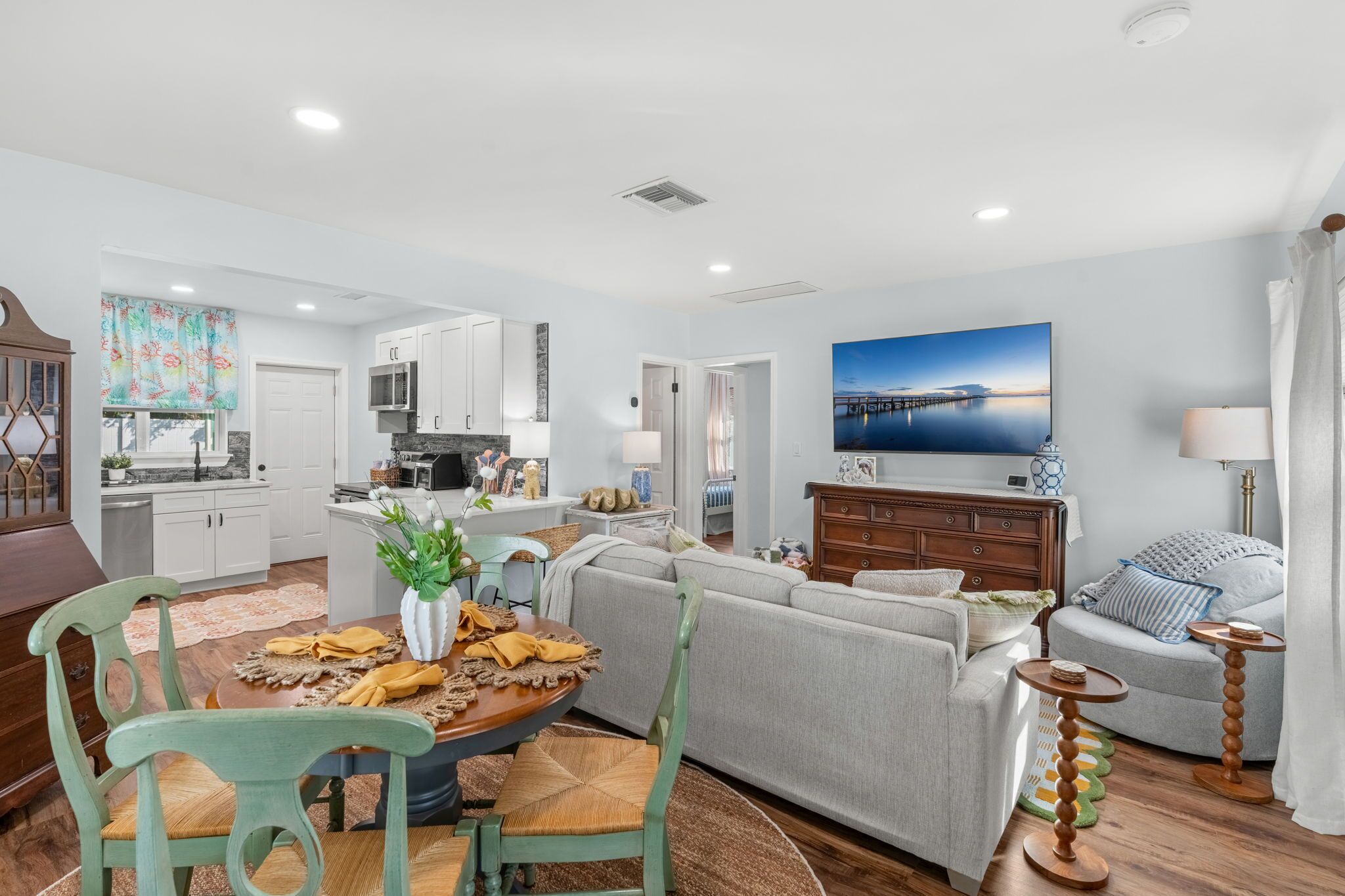 A modern living room with a dining area, a kitchen, and a large window with a view of a bridge.