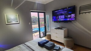 Una habitación de hotel con una cama, un televisor montado en la pared, un armario pequeño y una puerta corrediza de vidrio que da a un espacio exterior.