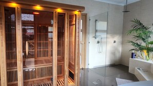 Una sauna de madera tradicional con puertas correderas, un box de ducha de vidrio y una planta en maceta a la derecha.