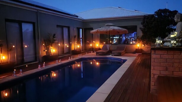 Piscina con una tumbona y una estatua, rodeada de iluminación cálida y un muro de ladrillo.