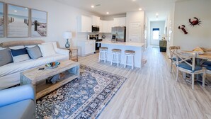 A modern kitchen with white cabinets, a central island with stools, and a dining area with wooden chairs and a table. - Coastal Retreat Just Steps From the Beach 🌴 (Port St. Joe)